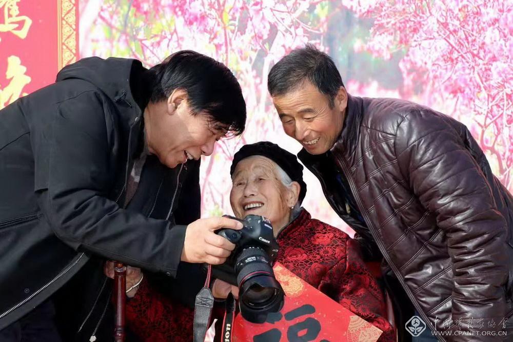 6.陆占林（左）向陇城镇村民展示全家福作品。刘平原摄.jpg