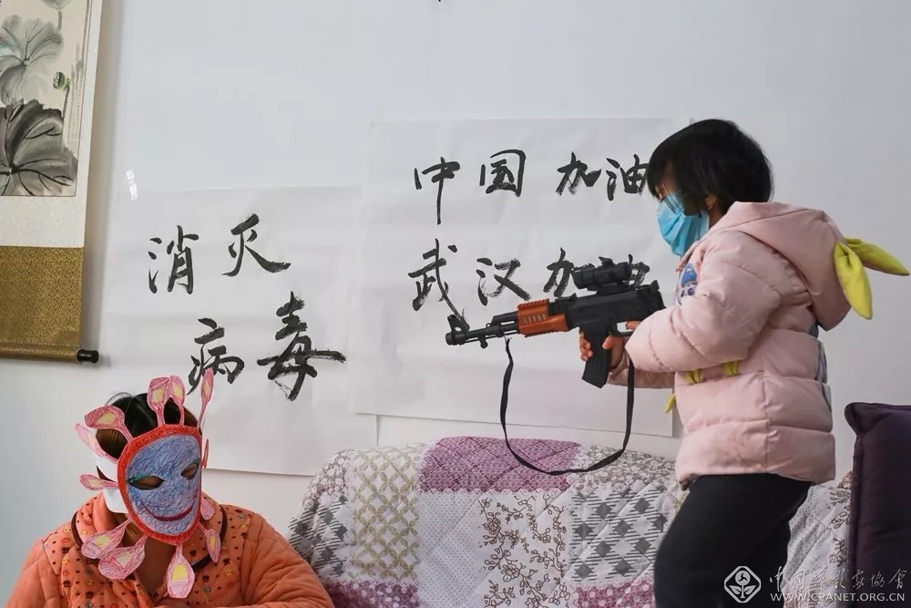 19.宅在家里，每天都能听到，抗击病毒的广播声音，电视画面。爸爸妈妈同宁宁一起画画、剪成帽子戴在妈妈的头上，小宁宁正用玩具枪消灭病毒。叶小平摄 选自重庆摄协《2020“抗疫”宅家日常生活摄影作品集》.jpg